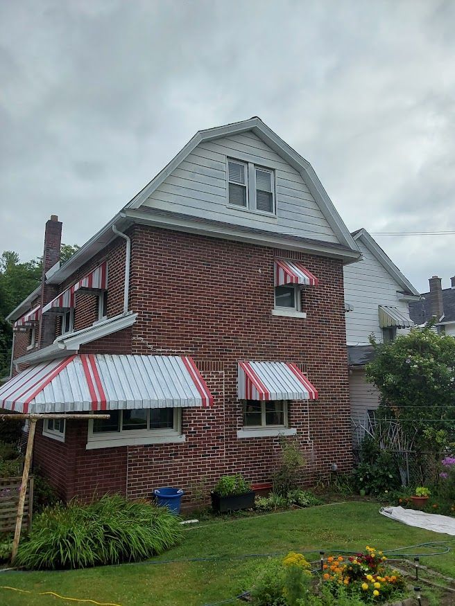 A brick house with red and white awnings on the windows.