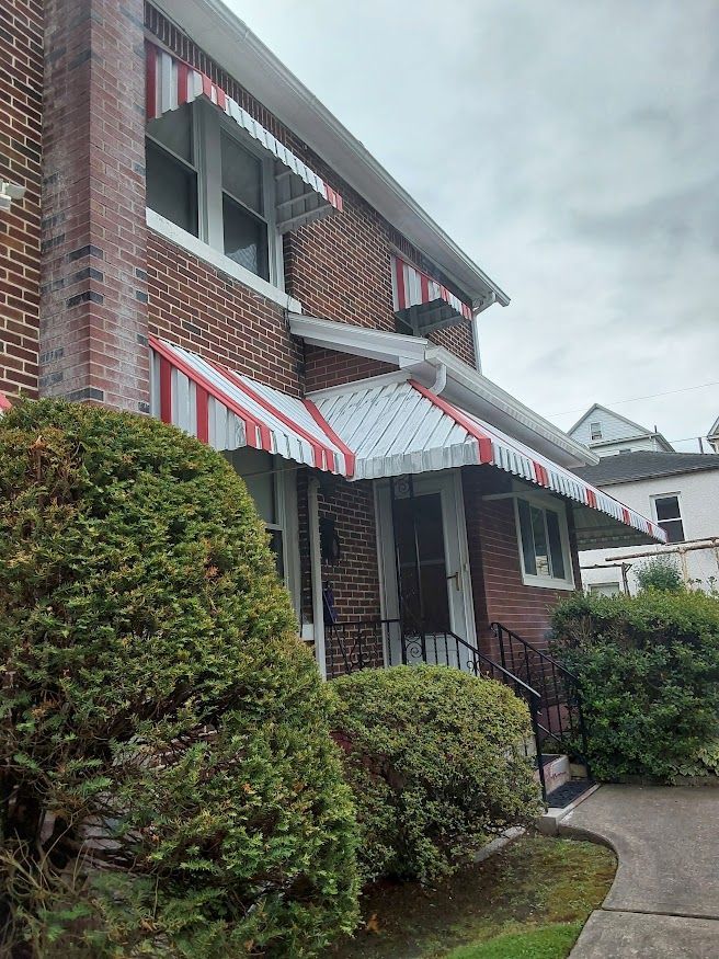 Red and white striped awnings over a brick house with green bushes in front.