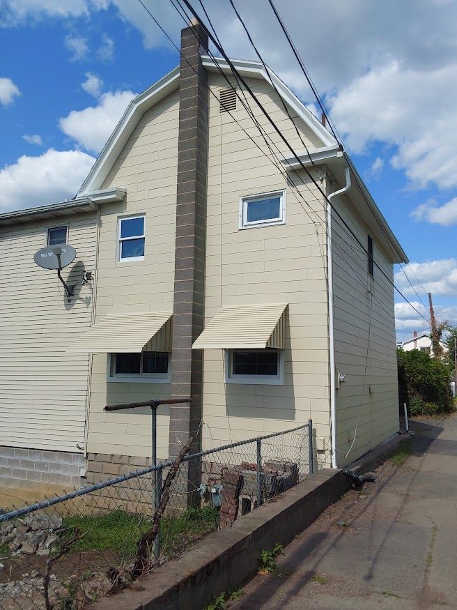Side view of a two-story beige building with a brick chimney. Two awnings are over windows.