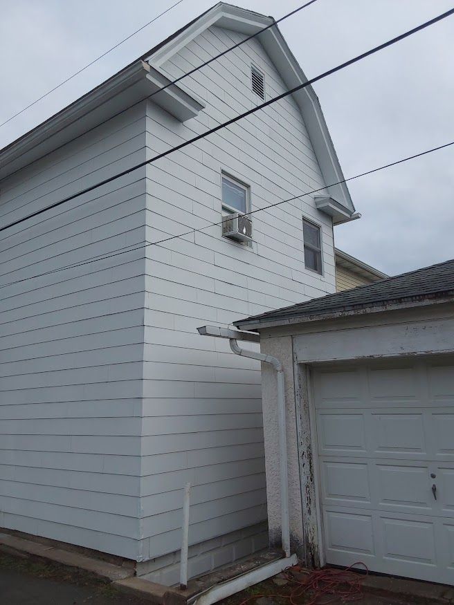 White house with a garage attached; two stories, an air conditioner is in the window.