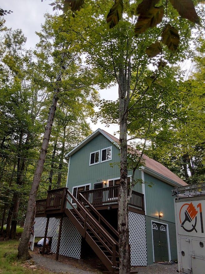Two-story, teal house with brown deck and stairs surrounded by trees.