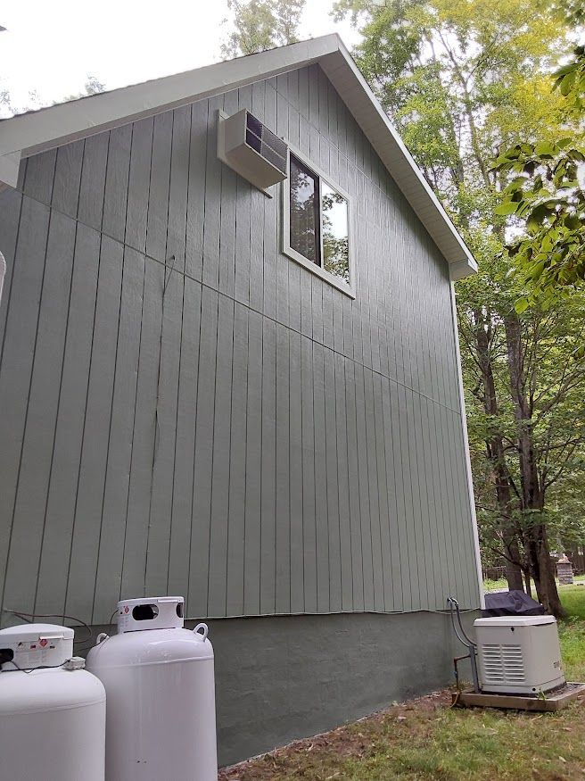 Side of a gray building with window, AC unit, propane tanks, and generator outside.