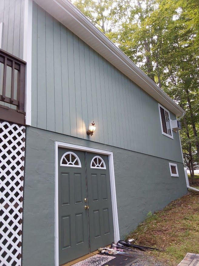 Side of a house with green siding and doors, white trim, and a latticework base.