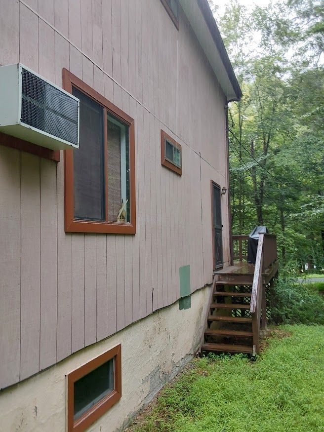 Side of a two-story house with brown trim, windows, stairs. Air conditioner unit attached to the wall.