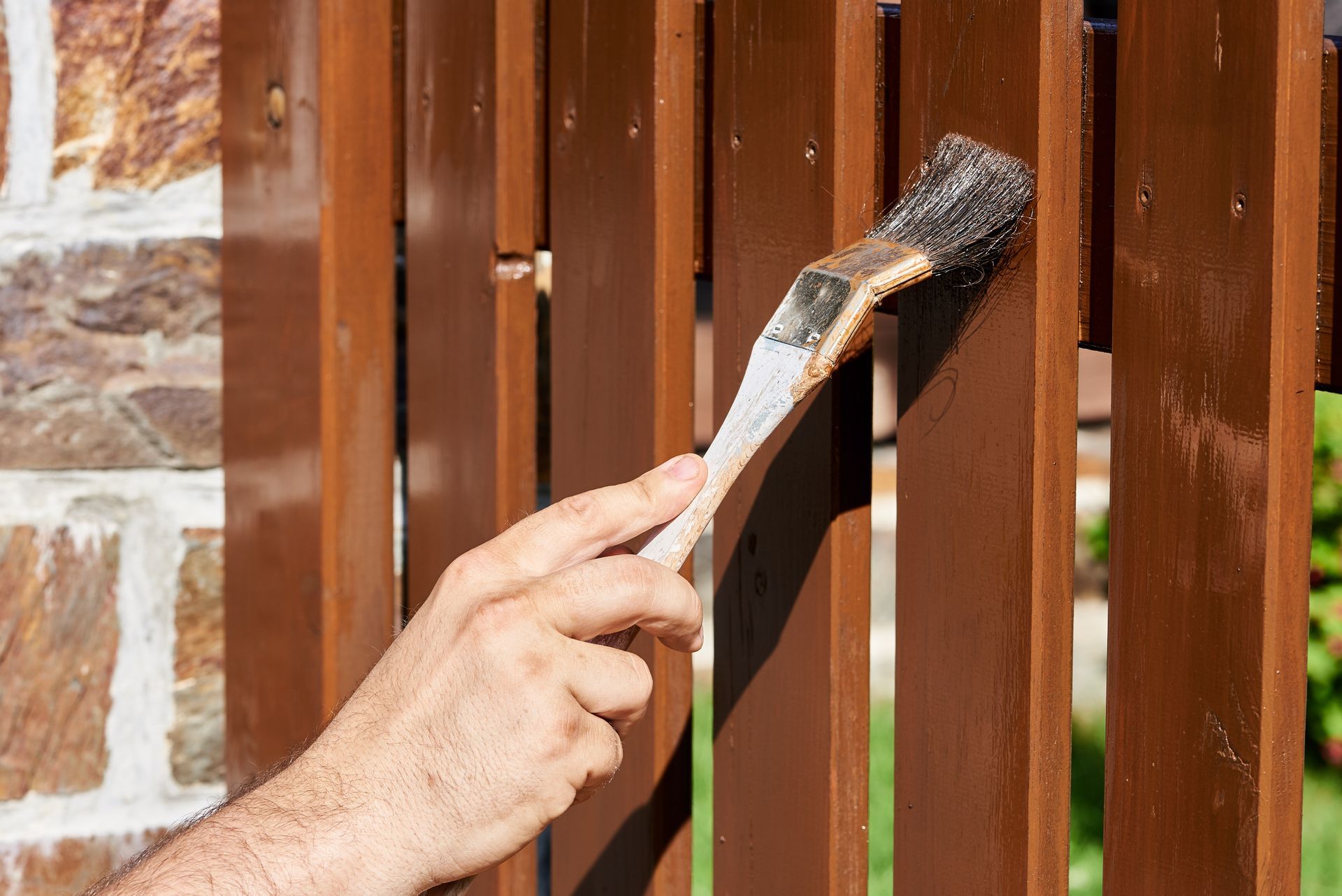 A person is painting a wooden fence with a brush.