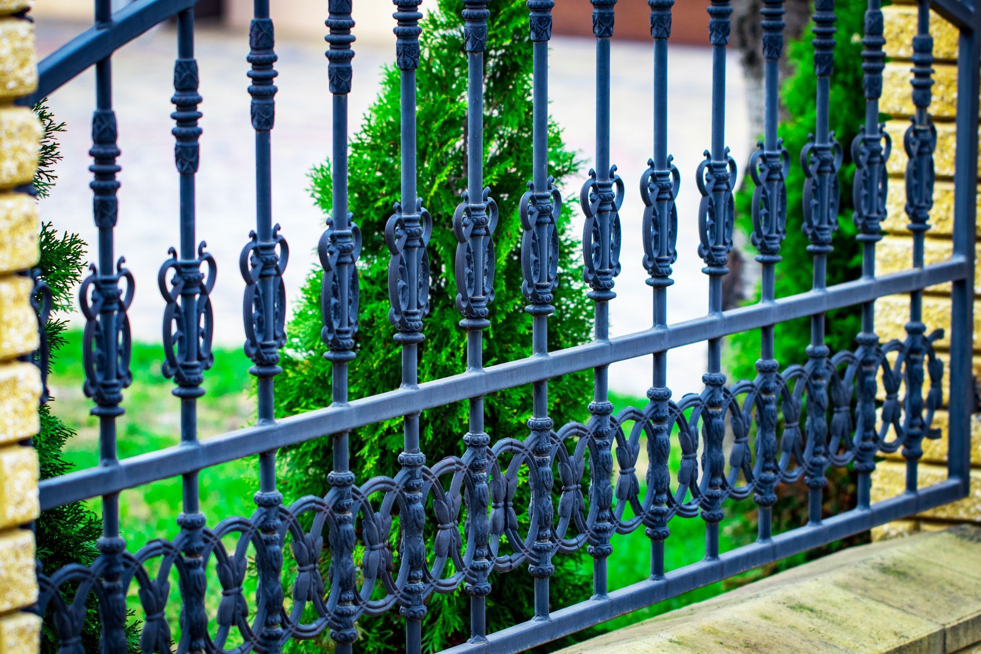 A close up of a wrought iron fence with trees in the background.