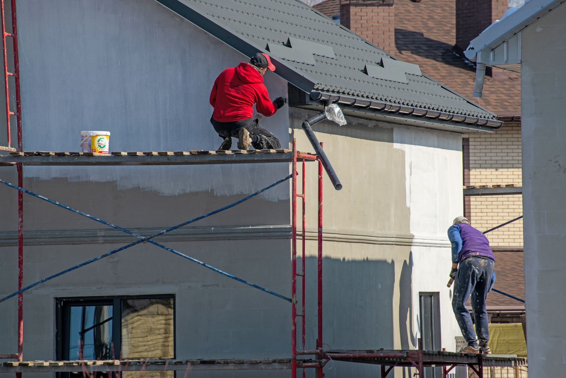 Two men are painting the side of a house on a scaffolding.