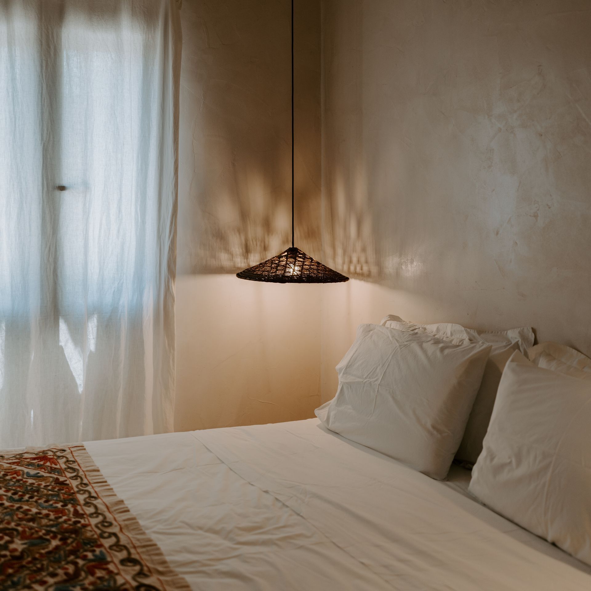 A bed with white sheets and pillows in a bedroom next to a window.