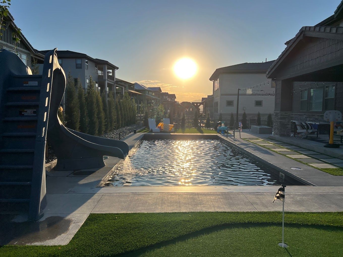 A swimming pool with a slide and a putting green in front of a house.