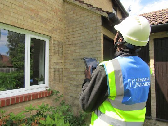 Worker in a hard hat and reflective vest using a tablet beside a house window
