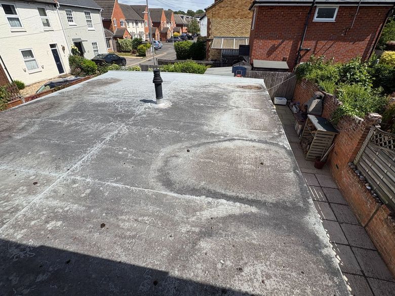 Flat rooftop terrace with a vent pipe, overlooking neighboring houses and a street.