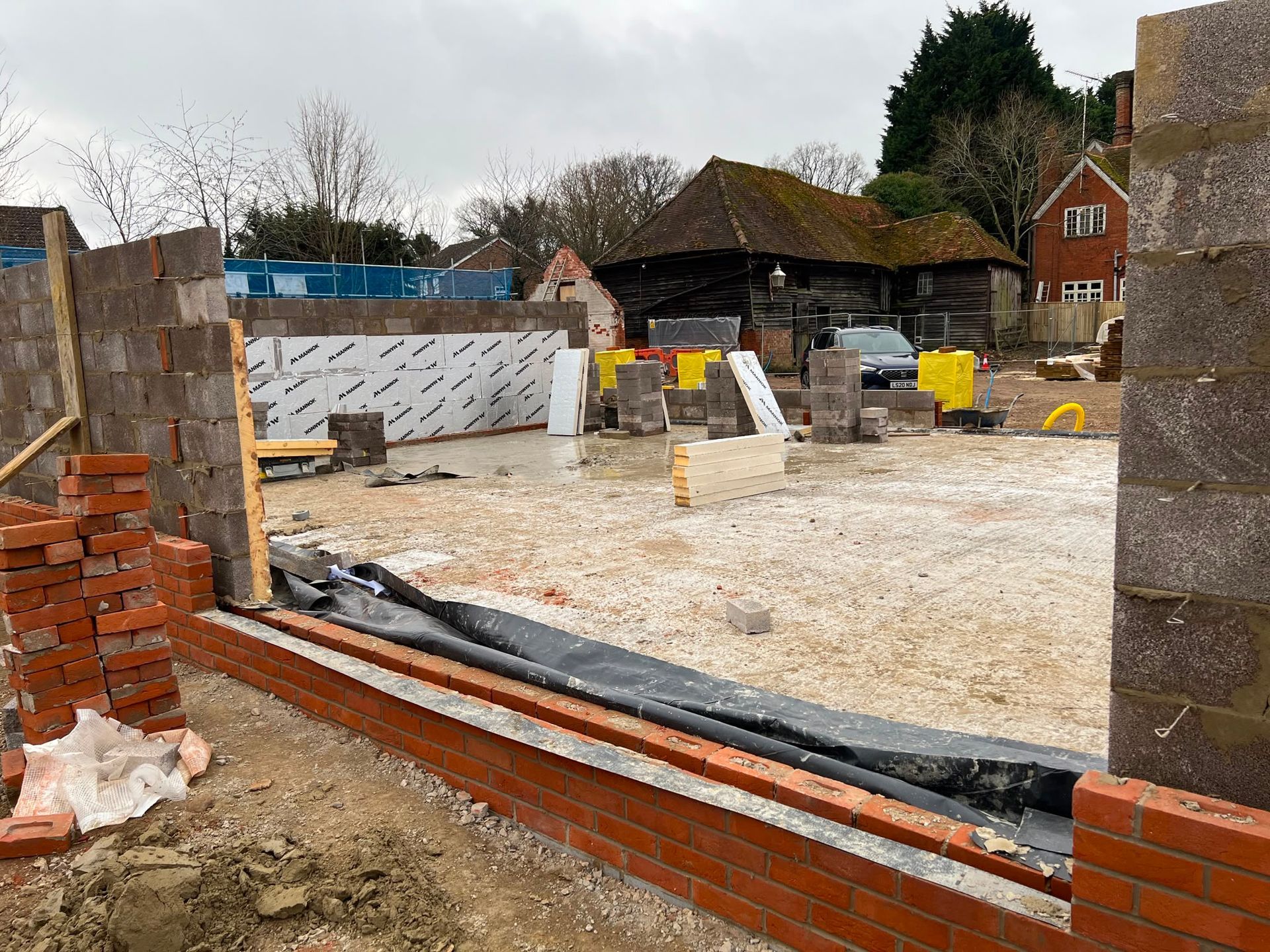 Construction site with brick wall, gravel ground, yellow equipment, and workers in the distance