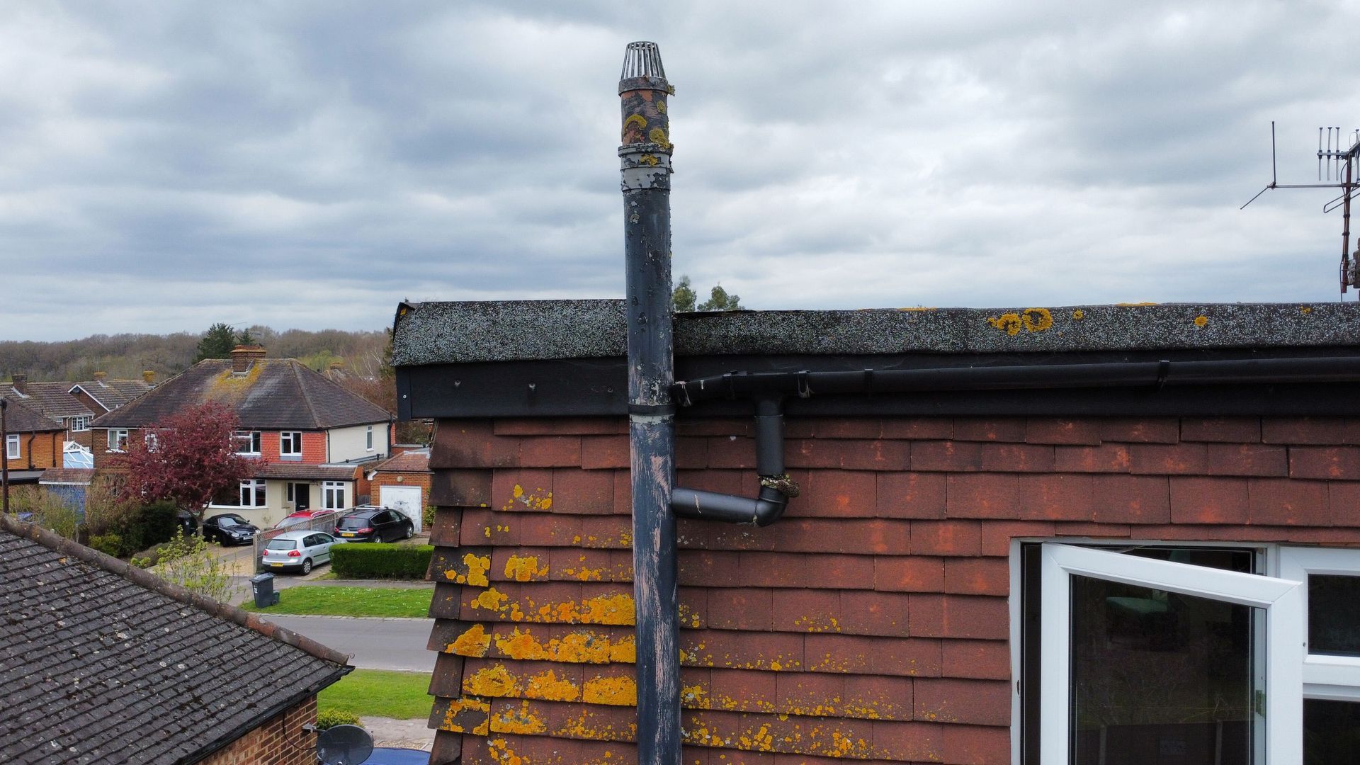 Rooftop and chimney on a red-brick house overlooking a cloudy suburban street