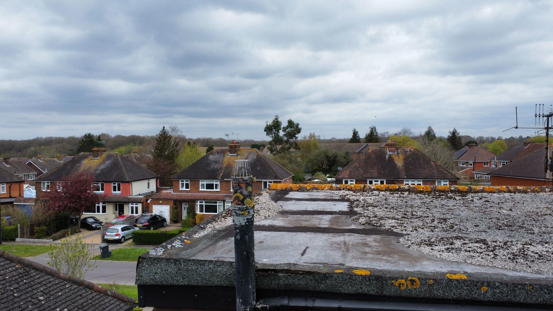 Suburban neighborhood with houses, parked cars, and a stone wall under a cloudy sky