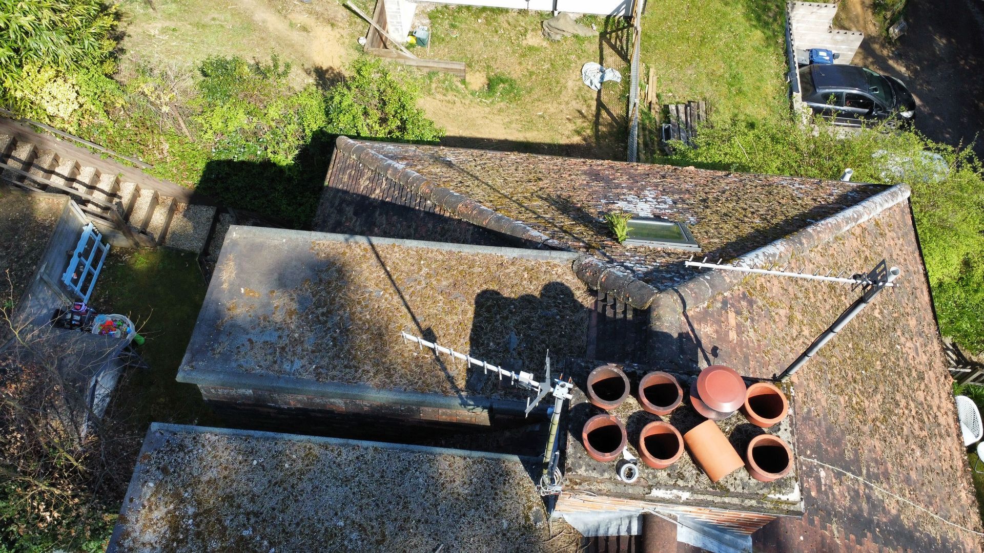 Aerial view of a rooftop with satellite dish, terracotta pots, and surrounding greenery.