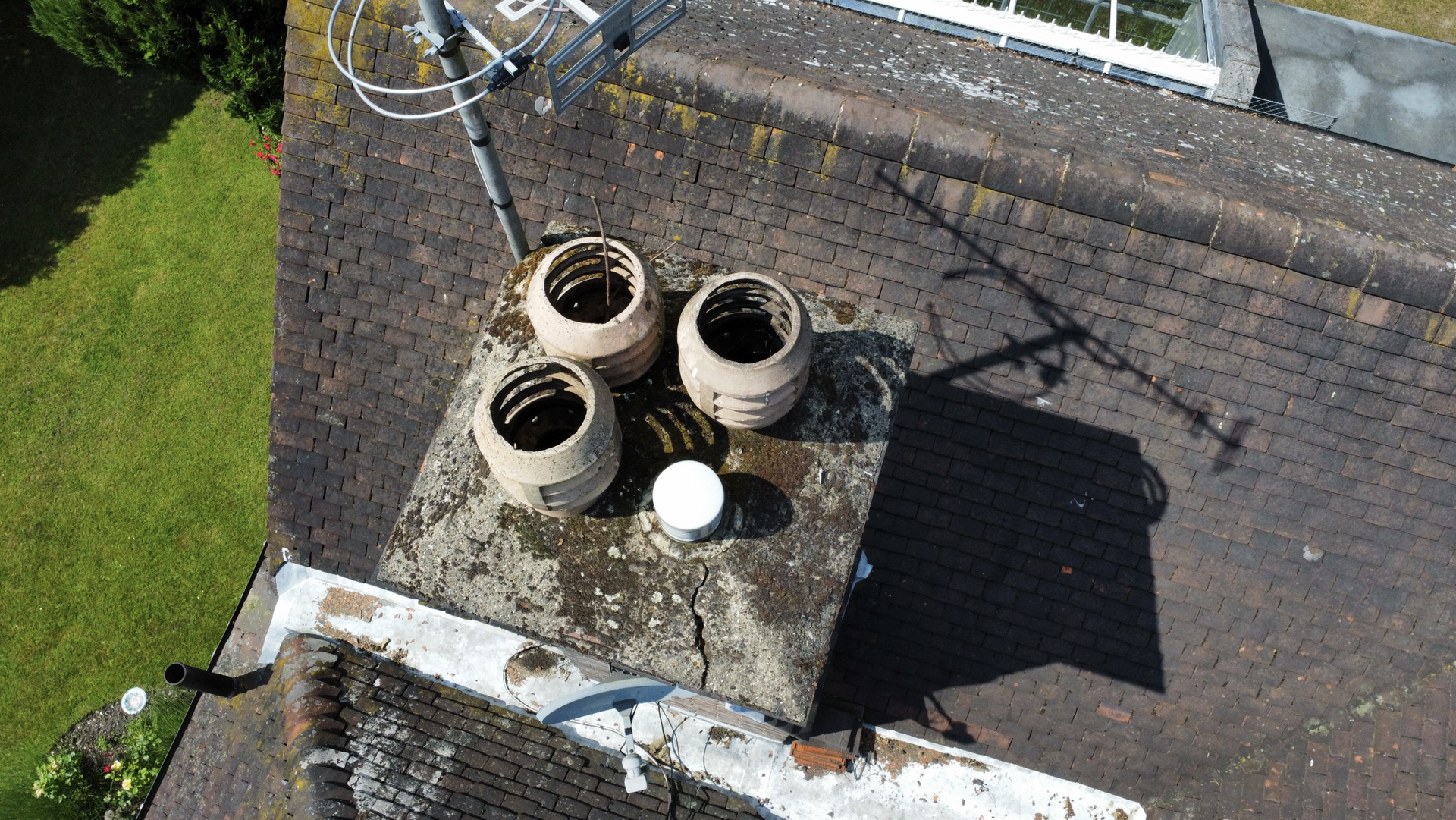 Rooftop with three round chimneys on a weathered shingle roof beside a grassy yard.