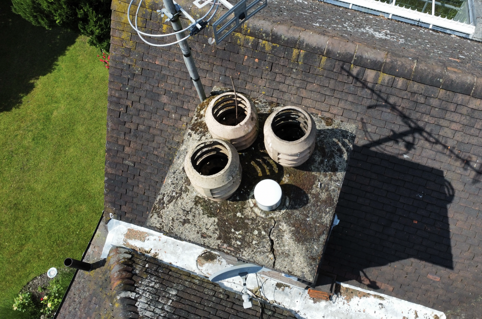 Aerial view of three rooftop vent pipes on a weathered chimney beside a grassy yard.