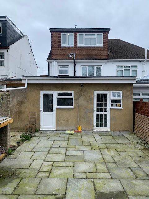 Back patio with paving stones and a white rear extension on a two-story house