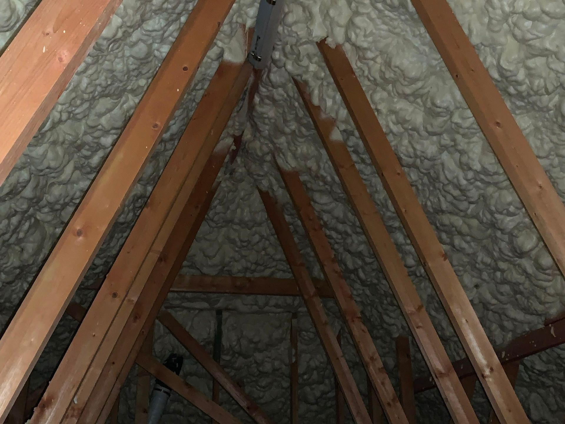 Attic rafters lined with spray foam insulation between wooden beams