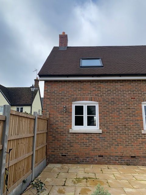 Backyard patio with brick house wall, white window, skylight, and wooden fence under cloudy sky