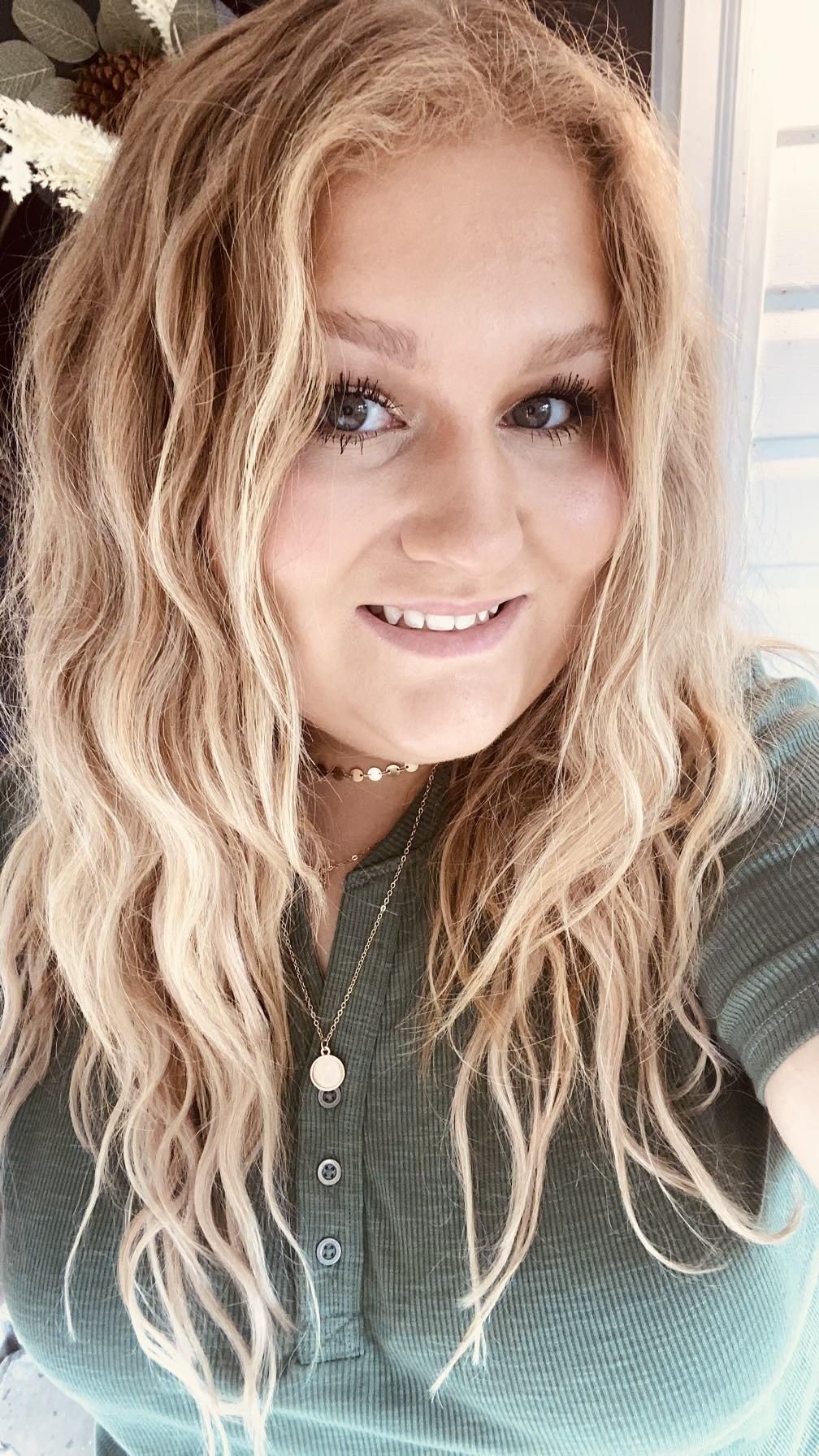 A woman with blonde hair is smiling and wearing a green shirt.