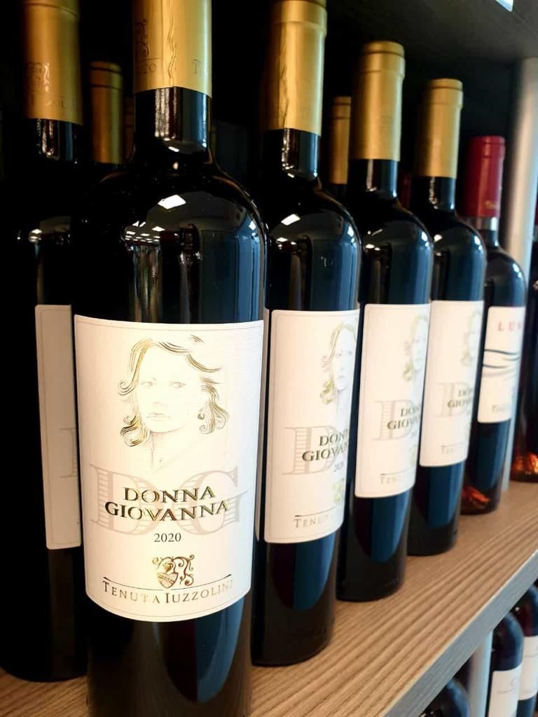 Una fila di bottiglie di vino Donna Giovanna sono allineate su uno scaffale.