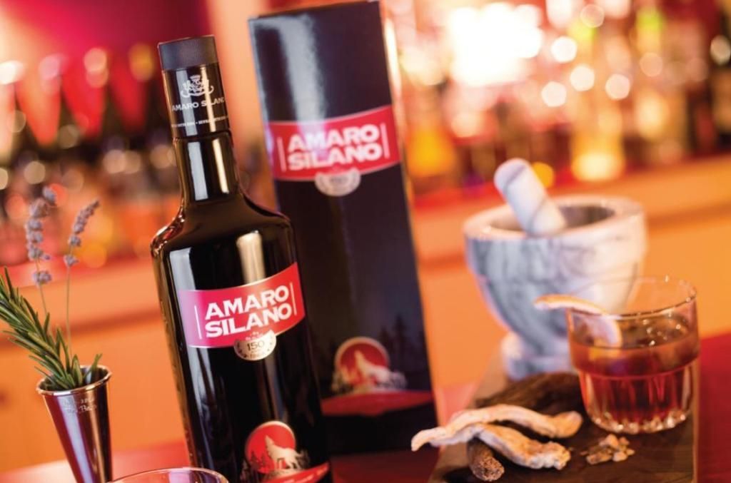 Una bottiglia di amaro silano è appoggiata sul bancone accanto a un bicchiere.