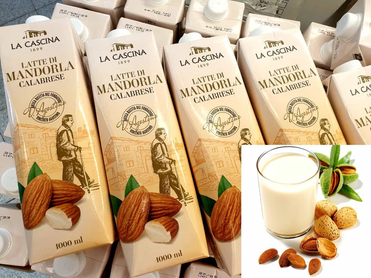 Un bicchiere di latte di mandorle è accanto a un mucchio di scatole di latte di mandorle