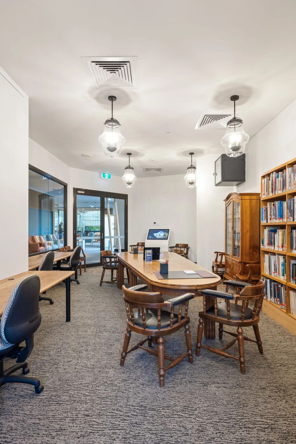 Library with large wooden table, chairs, bookshelves, and pendant lights.