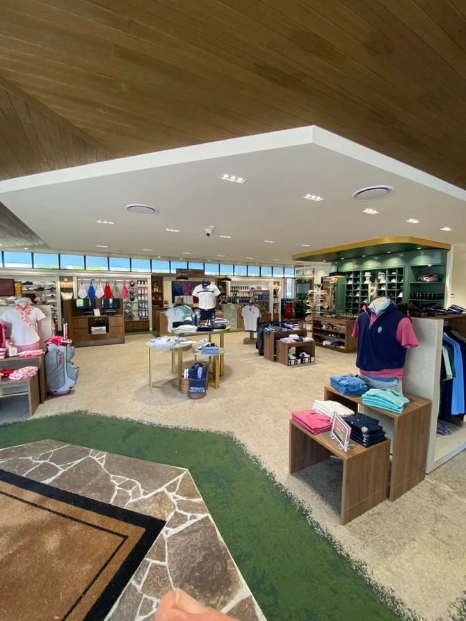 Interior of a golf shop with clothing displays. Brightly lit, with wood accents and a grass-like carpet.