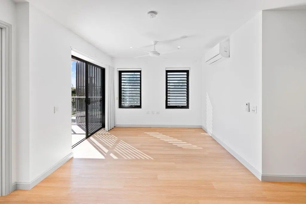 Empty room with hardwood floors, white walls, black windows and sliding door, ceiling fan.