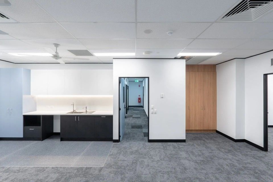 Empty office space with kitchenette and hallway, gray carpet, white walls.