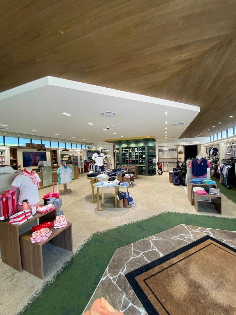 Interior of a golf shop with clothing displays, a central rug, and a textured ceiling.