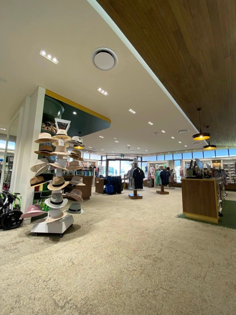 Inside a well-lit store, hats displayed on a stand. Clothing racks and a counter visible.