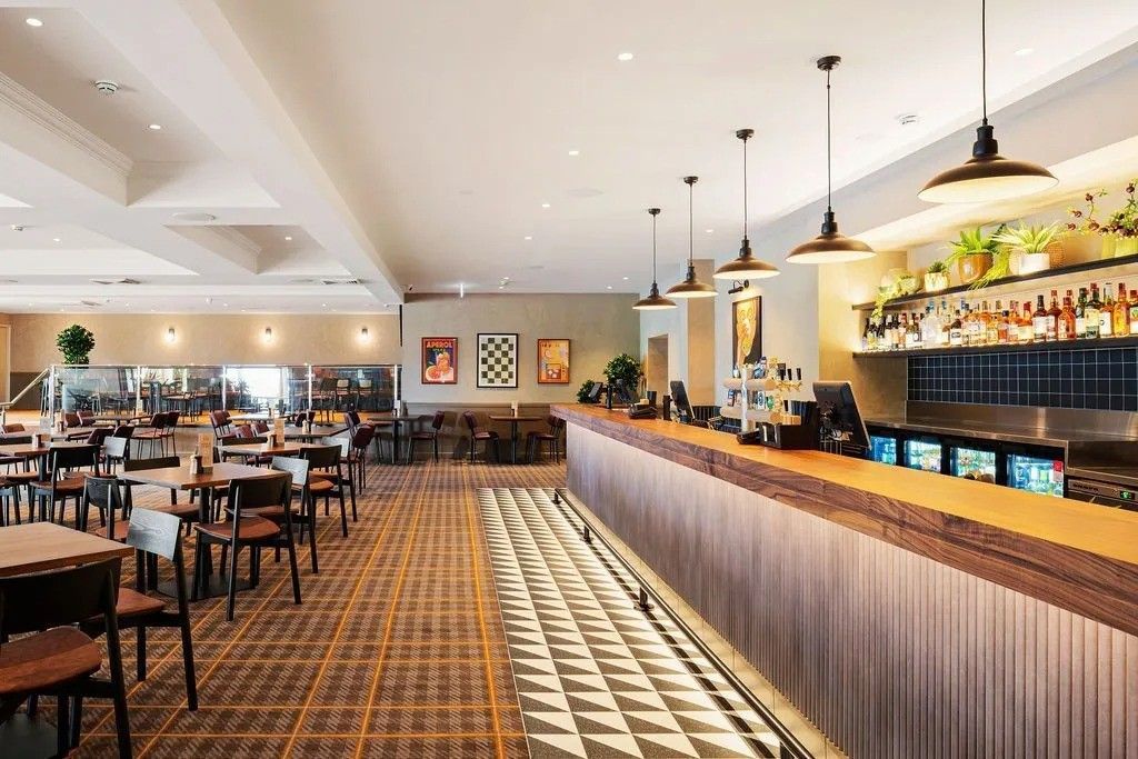Bar interior with a wooden bar, tables, chairs, and overhead lights.