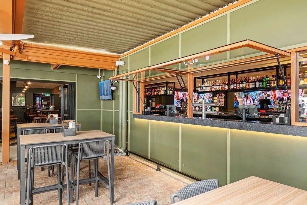 Outdoor bar with olive green paneling, wood accents, and metal tables. A bar with liquor bottles is visible.
