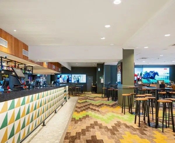 Bar interior with zigzag patterned floor, bar, stools, and TVs.