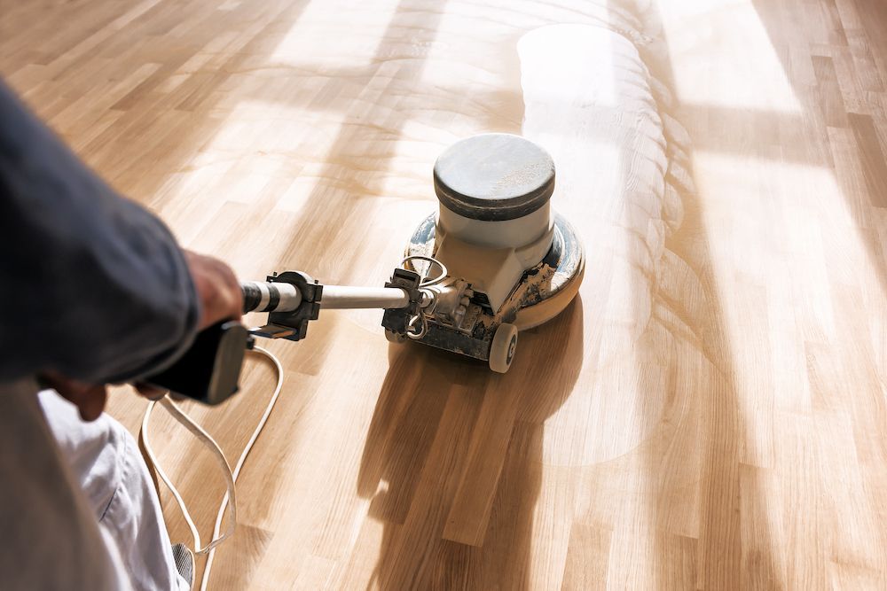 A Person is Using a Machine to Polish a Wooden Floor — Coastline Floor Sanding in Gosford, NSW
