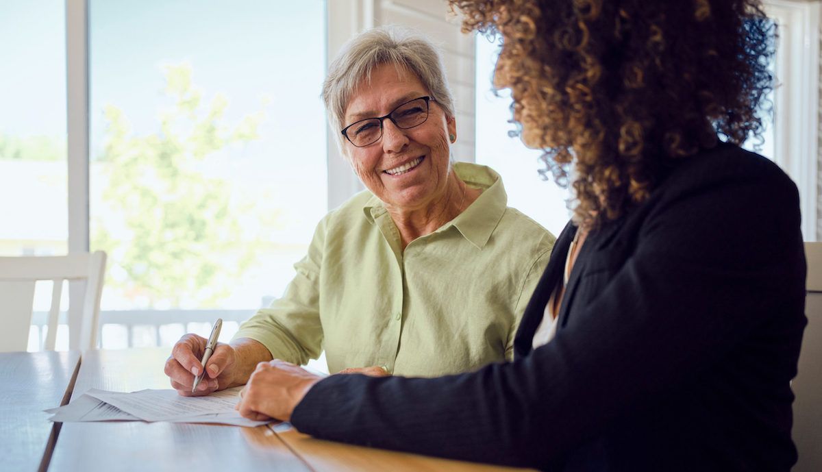 Two people talking at a table, smiling in a bright office setting.