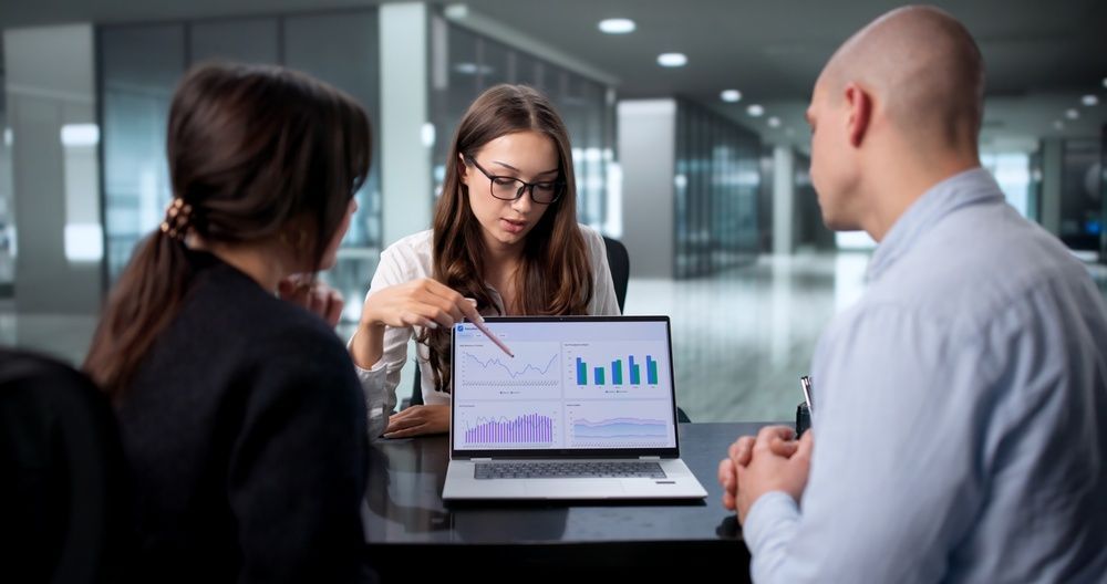 Colleagues discussing a bar chart on a laptop in a modern office meeting room