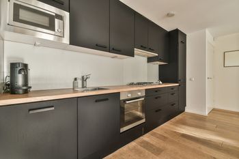 Modern kitchen with black cabinets, wood countertops, stainless appliances, and light wood floors