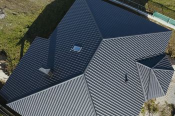 Aerial view of a gray shingled roof with skylights and vents beside a grassy yard.