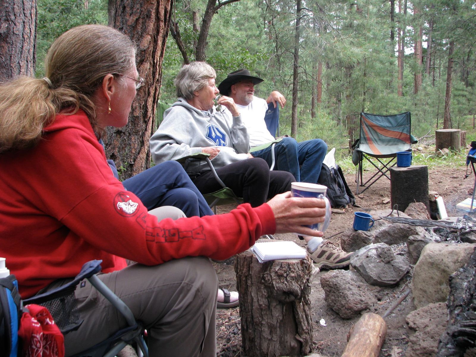 People sitting around a campfire in folding chairs in a wooded campsite