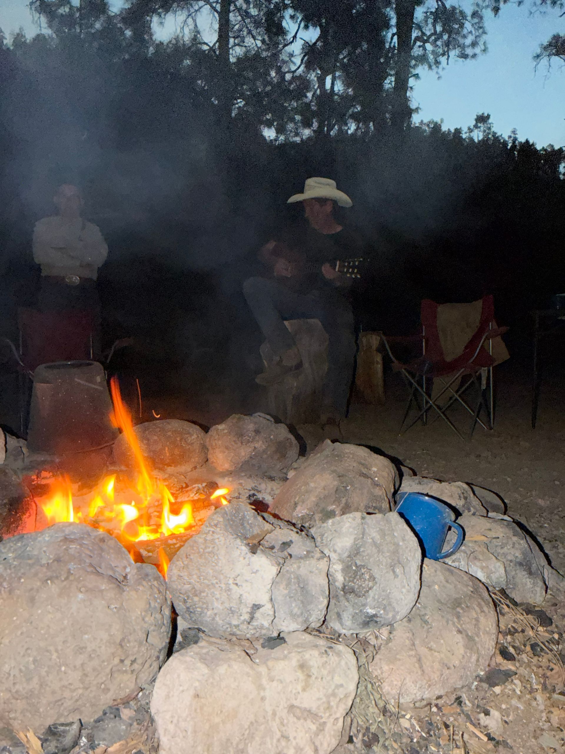 People sitting around a campfire behind a ring of large rocks at dusk