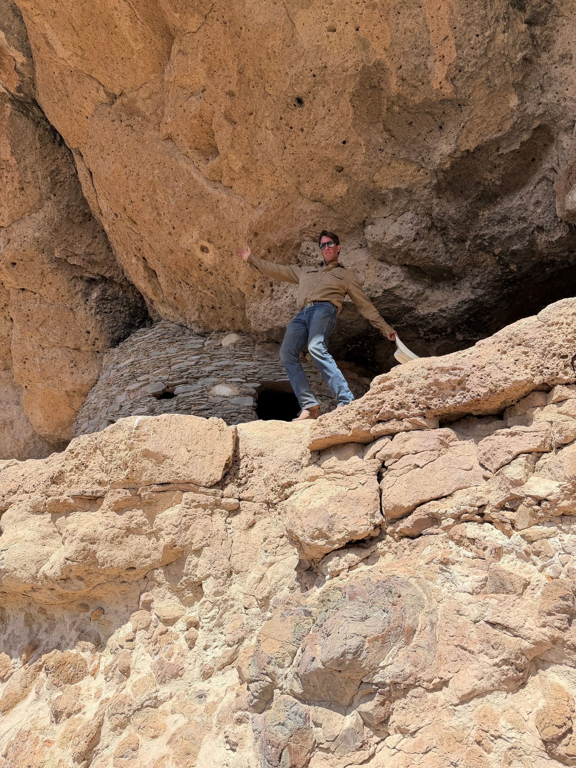 Person standing under a large rock overhang in a desert-like rocky landscape.