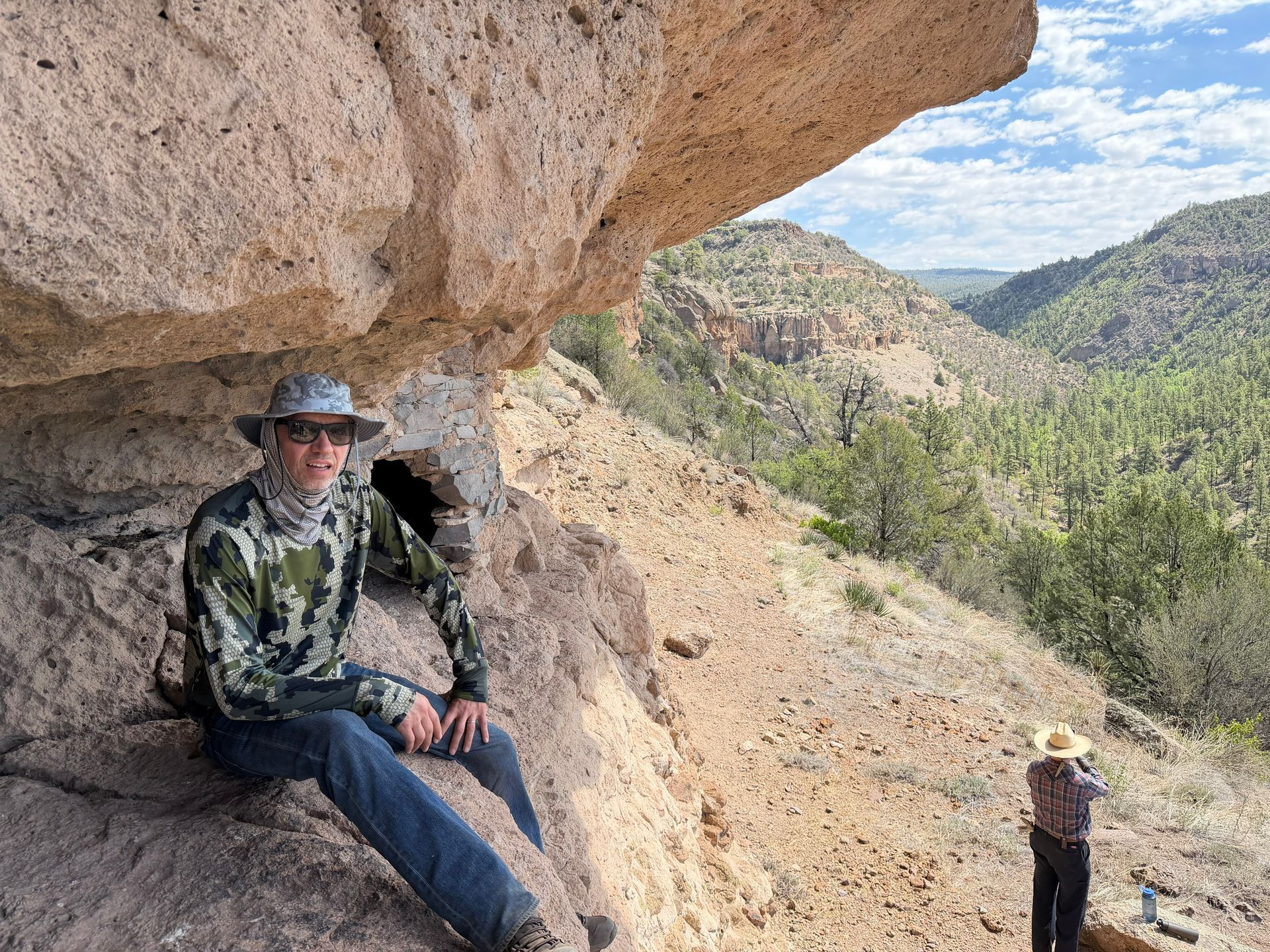 Hiker sitting under a rock overhang with a mountain valley in the background