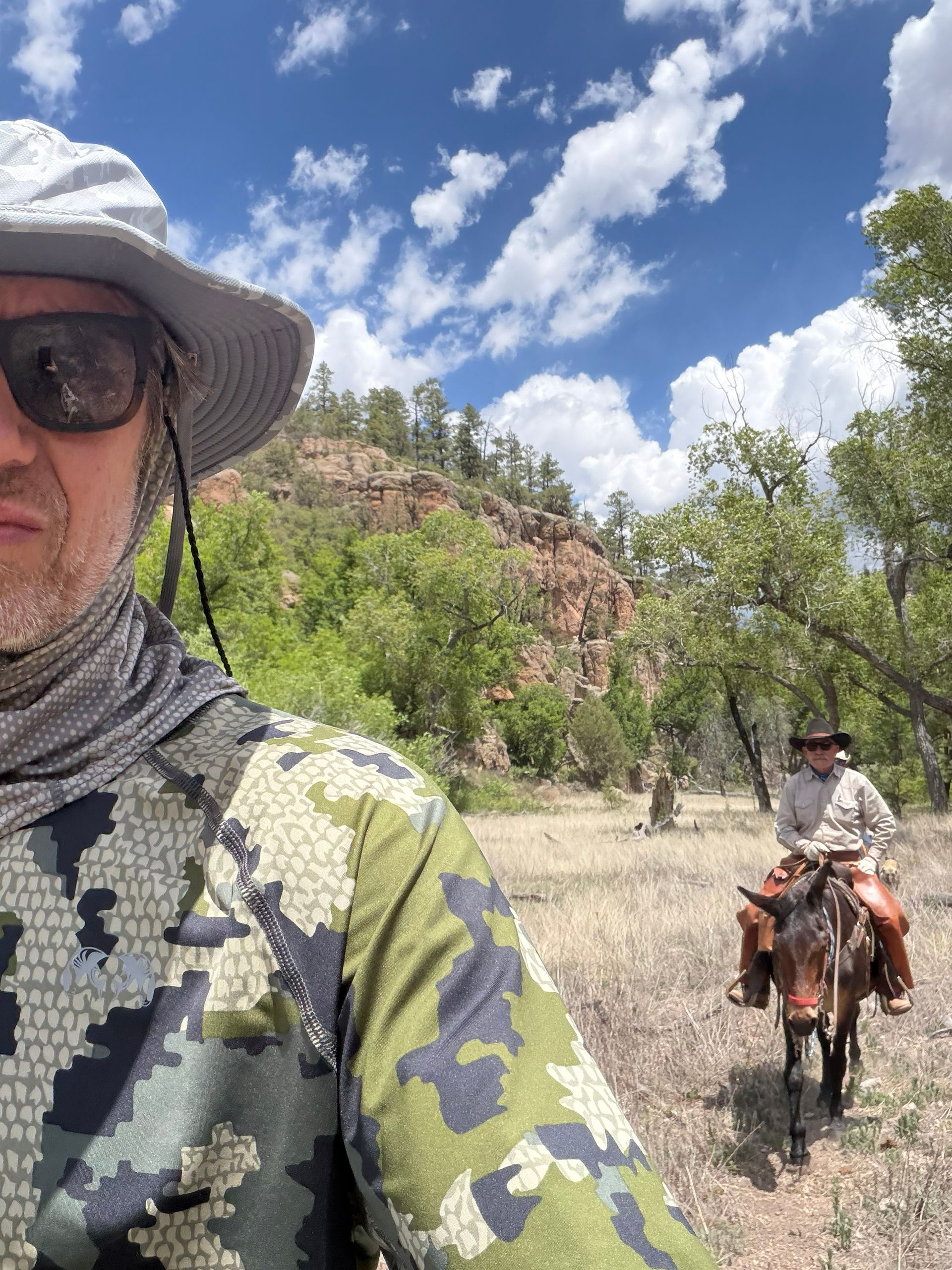 Two riders on horseback in a rocky desert under a blue sky with clouds