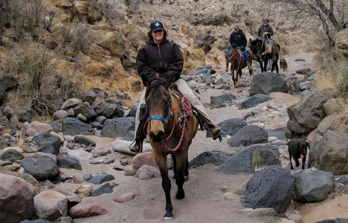 People on horseback riding on a rocky trail in a canyon.