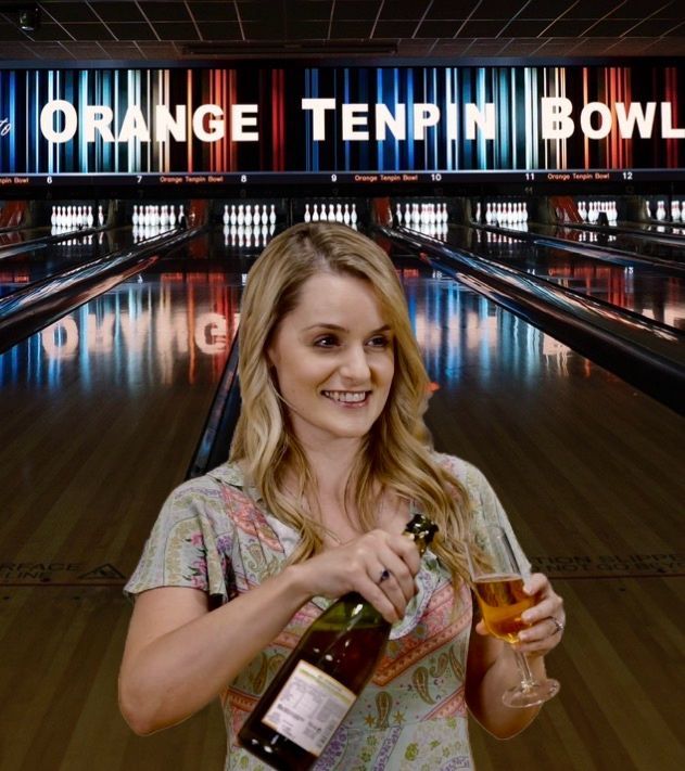 Woman pouring wine at a bowling alley with a bright Orange Tenpin Bowl sign in the background