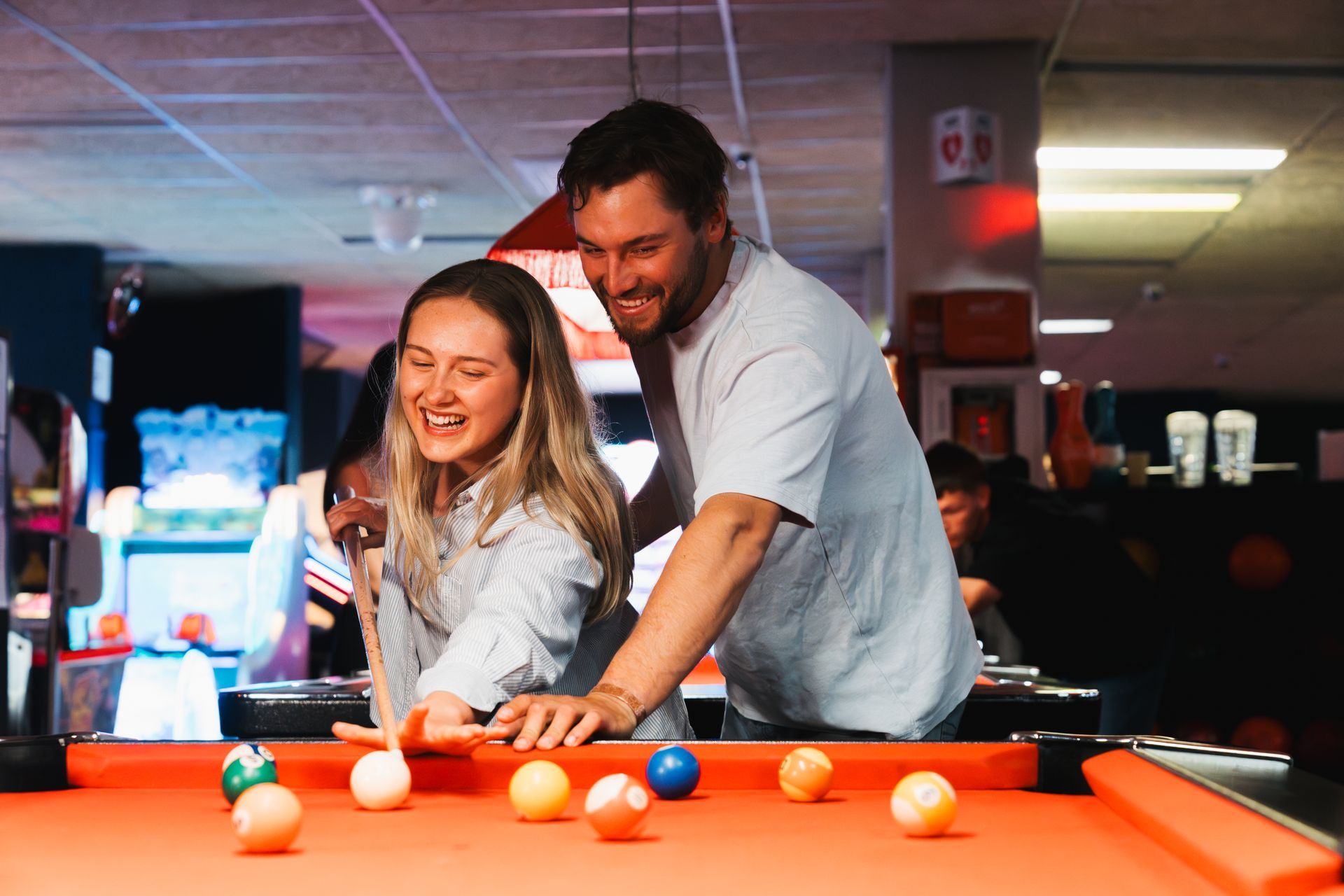 Two People Smiling and Playing Pool at an Orange Billiards Table in a Dimly Lit Bar — Orange Tenpin Bowl in Orange, NSW